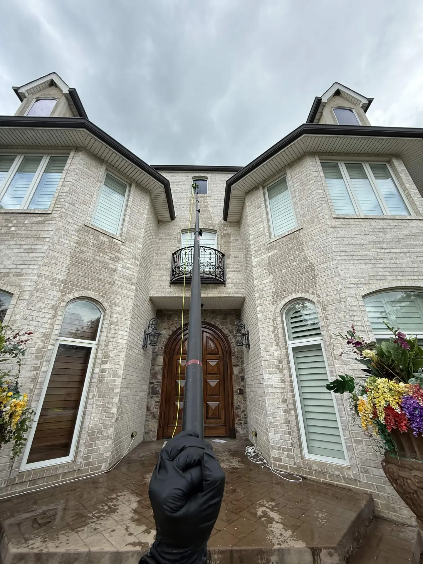 Mist Window Cleaning technician using a water-fed pole on a tall brick home